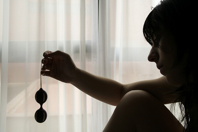 Mujer a contraluz, sentada, mirando y sujetando unas bolas chinas