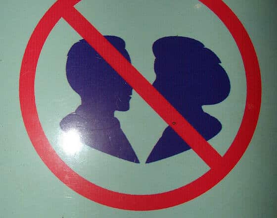 Sobre fondo verde, aparece el perfil en negro de un hombre y una mujer, uno frente a otro dentro de la señal de prohibido.
