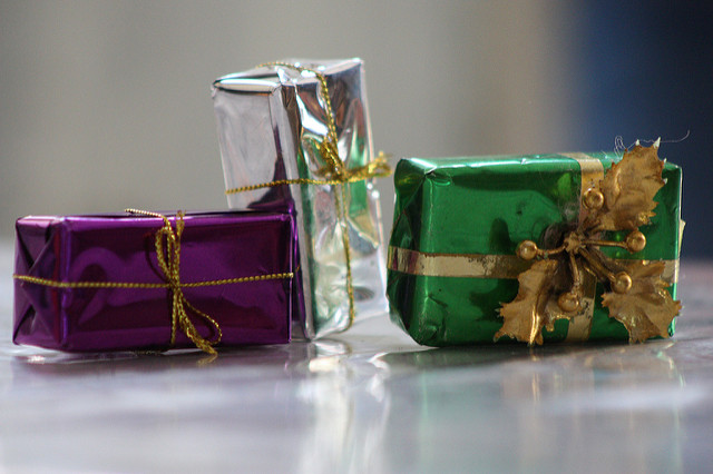 Tres cajas de regalo envueltas en distintos colores: morada, plata y verde