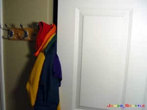 Una puerta blanca de armario entreabierta de la que sale la bandera del orgullo LGTB