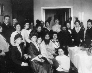 Foto en blanco y negro de Rasputín sentado en una silla y rodeado de mujeres.