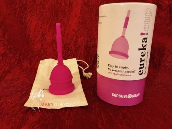Caja de embalaje de la Eureka! Cup junto a la copa de color rosa que está boca abajo sobre la funda blanca
