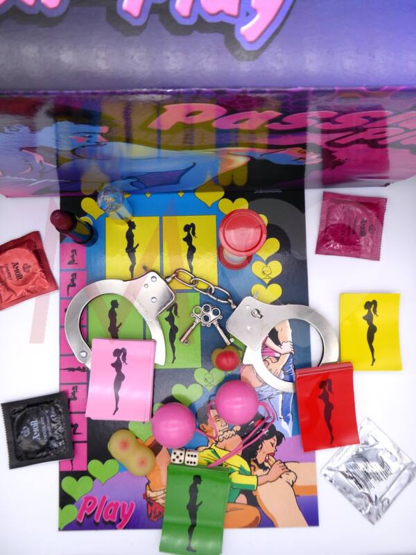 Contenido del juego Passion Play. Tablero, cartas-pruebas, esposas de metal y llaves, bolas chinas rosa, dados, reloj de arena, tres preservativos de sabores y monodosis lubricante.
