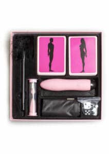 Caja de Passion Play de Secret Play donde se ve un vibrador rosa, un reloj de arena, cartas él/ella, dados, plumero negro y cinta de raso negra.
