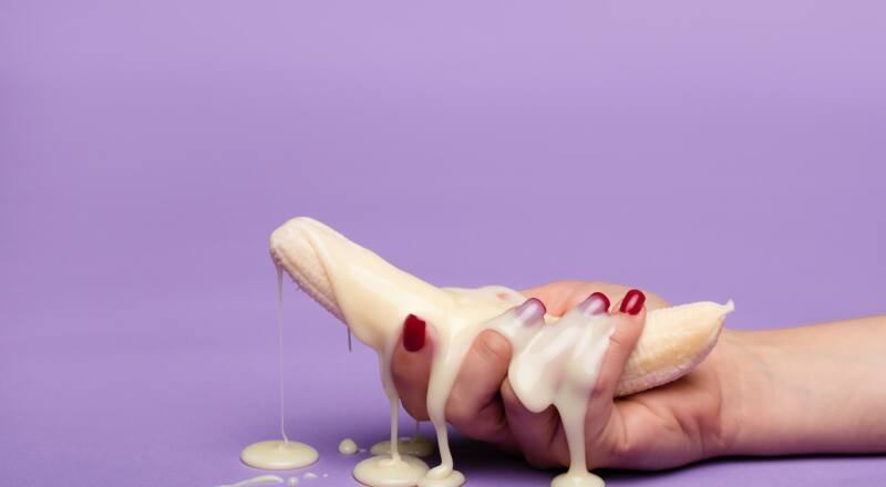 Plátano pelado lleno de leche condensada y agarrado por una mano femenina con las uñas pintadas de rojo