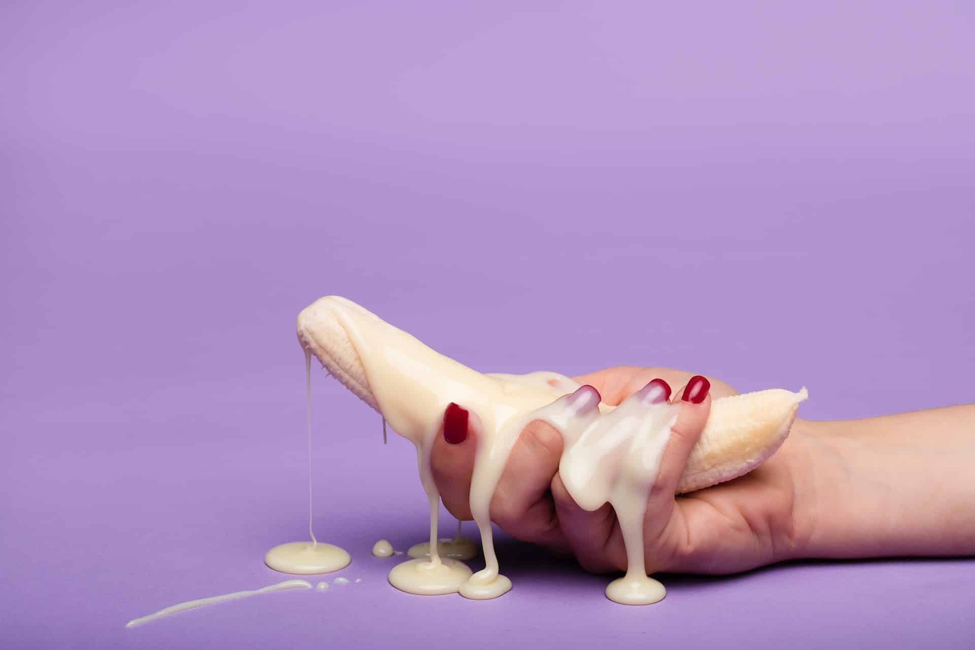 Plátano pelado lleno de leche condensada y agarrado por una mano femenina con las uñas pintadas de rojo