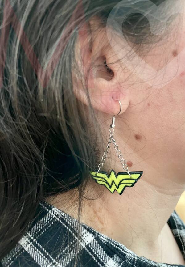 Pendientes logotipo Wonder Woman hechos a mano con polimer clay amarillo efecto neón y negro puestos en el lóbulo de la oreja.