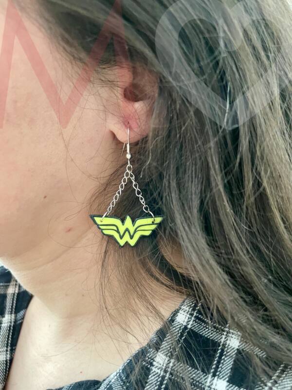 Pendientes logotipo Wonder Woman hechos a mano con polimer clay amarillo efecto neón y negro puestos en el lóbulo de la oreja.